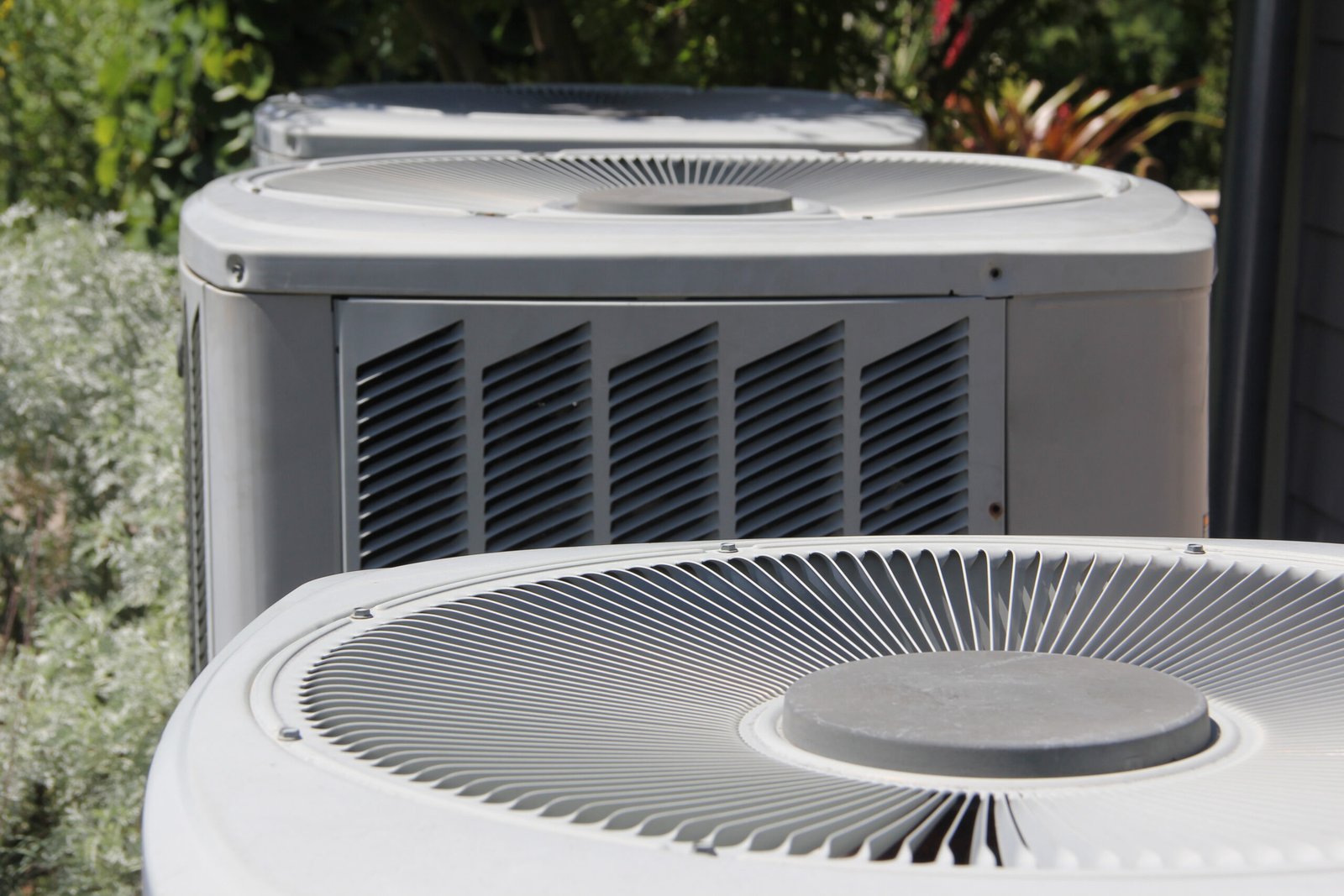 Outdoor air conditioning condenser units beside green foliage